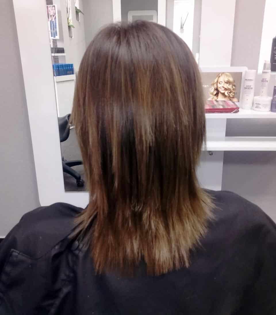Glattes, schulterlanges braunes Haar mit gleichmäßig geschnittenen Spitzen im hellen Friseursalon