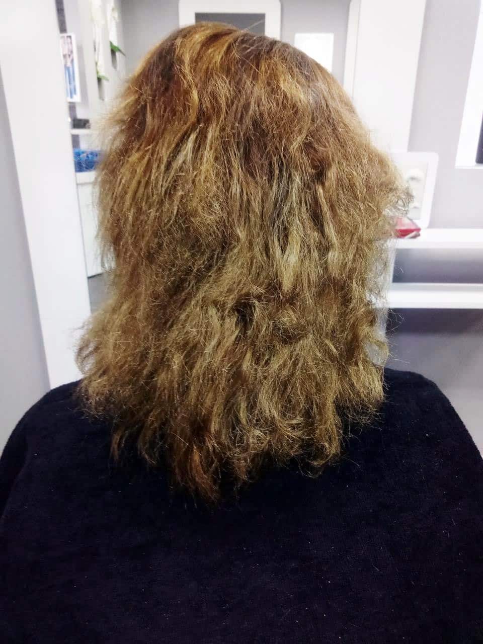 Welliges, trocken wirkendes Haar mit ausgefransten Spitzen Über einem schwarzen Umhang fällt welliges Haar in warmen Brauntönen mit trockener Struktur und ausgefransten Spitzen.
